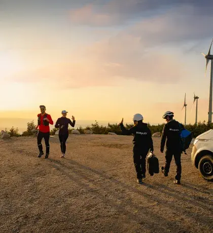 Joggeur et techniciens se saluant face à une éolienne