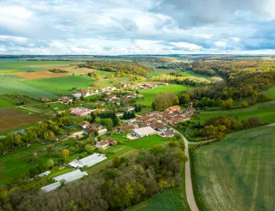 Photo aérienne d'une commune française avec quelques éoliennes visibles à l'horizon et des champs agricoles au premier plan